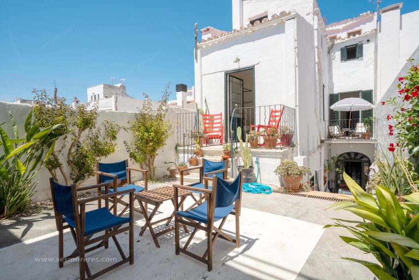 Patio soleado con mesa y sillas de exterior, plantas y fachada blanca en Menorca