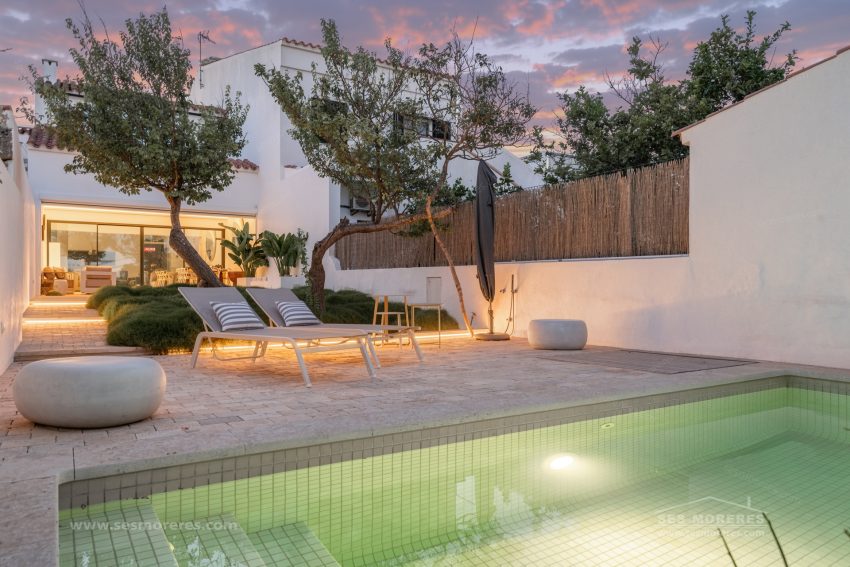 Patio ajardinado con piscina, árboles e iluminación cálida al atardecer en Menorca