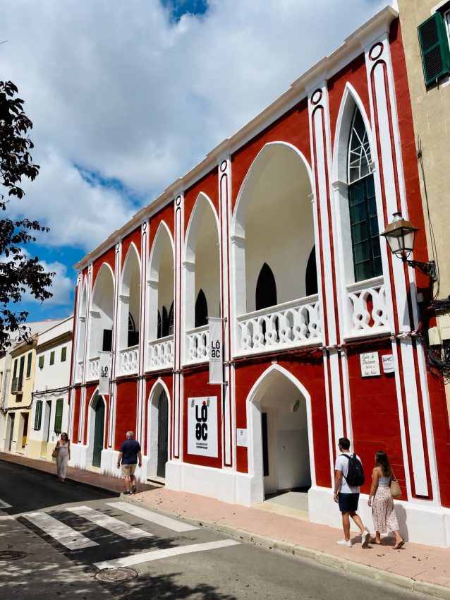 Fachada roja y blanca de LÔAC en Alaior con personas paseando