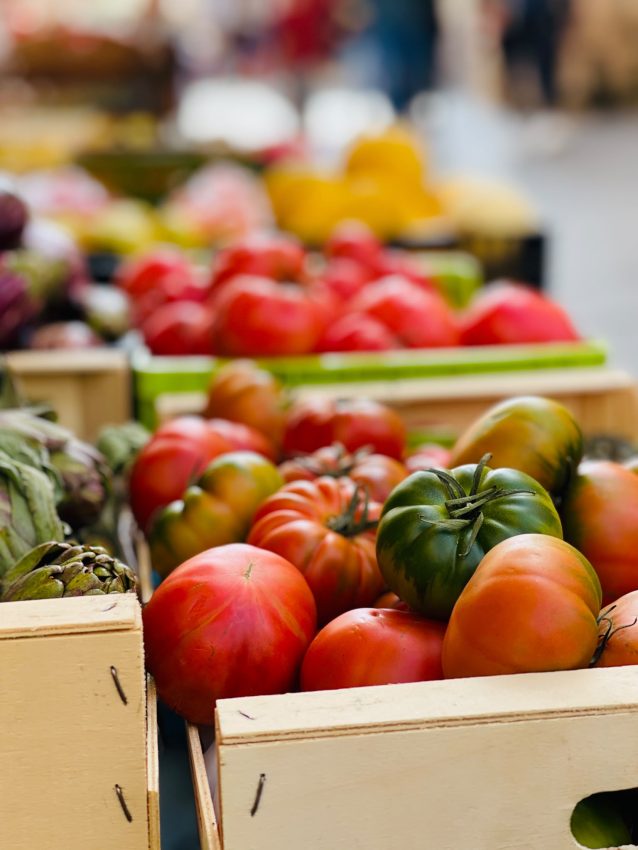 Tomates de distintos colores y verduras en cajas de un puesto de mercado