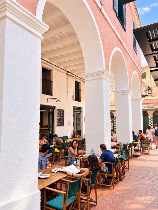 Terraza con mesas y sillas bajo grandes arcos blancos y rosados
