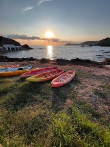 Colourful kayaks rest by the sea at sunrise in a peaceful Menorca cove. Colourful kayaks rest by the sea at sunrise in a peaceful Menorca cove.