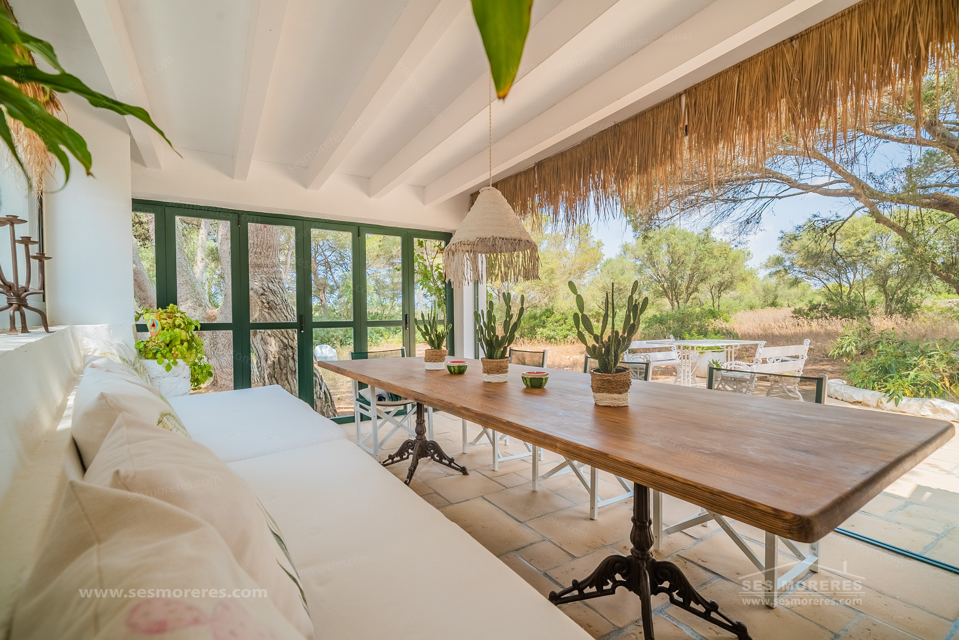 Covered terrace at a Menorcan country house with a wooden dining table overlooking trees