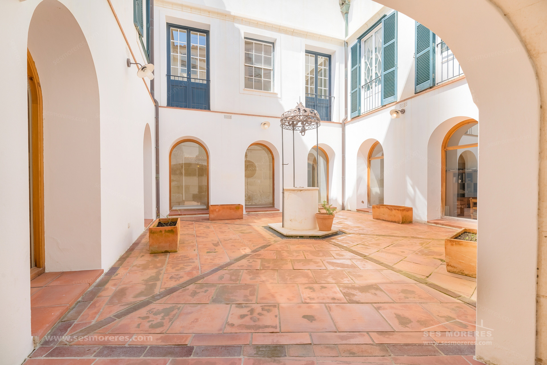 Courtyard of a house in Menorca with arches, terracotta tiles and green shutters